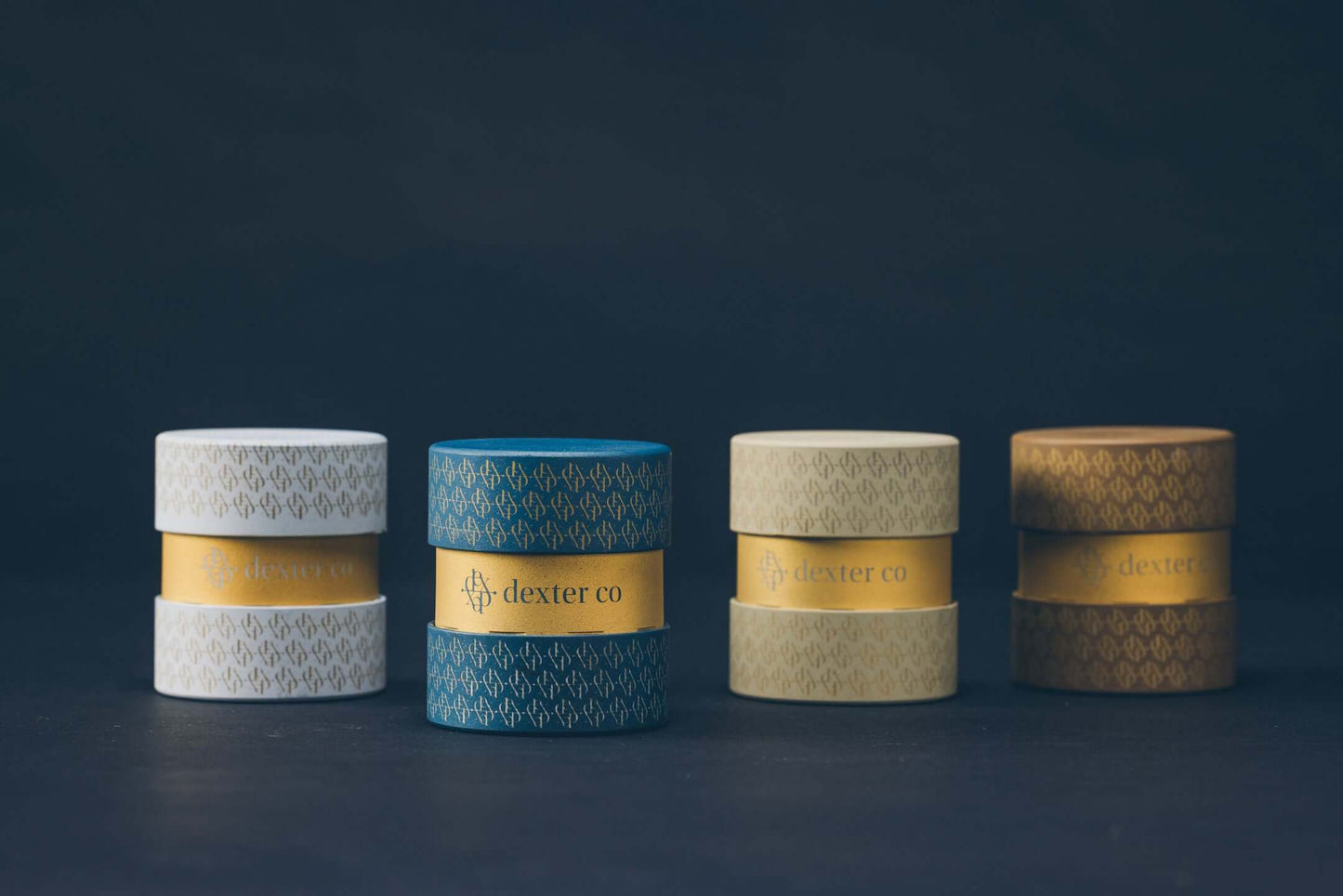 Stylish stacked jars from Dexter Co in white, blue, beige, and gold against a dark background.