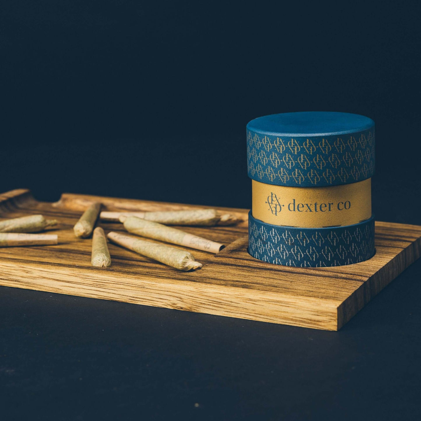 Dexter Co premium cannabis container on a wooden tray with rolled joints, showcasing luxury smoking accessories.