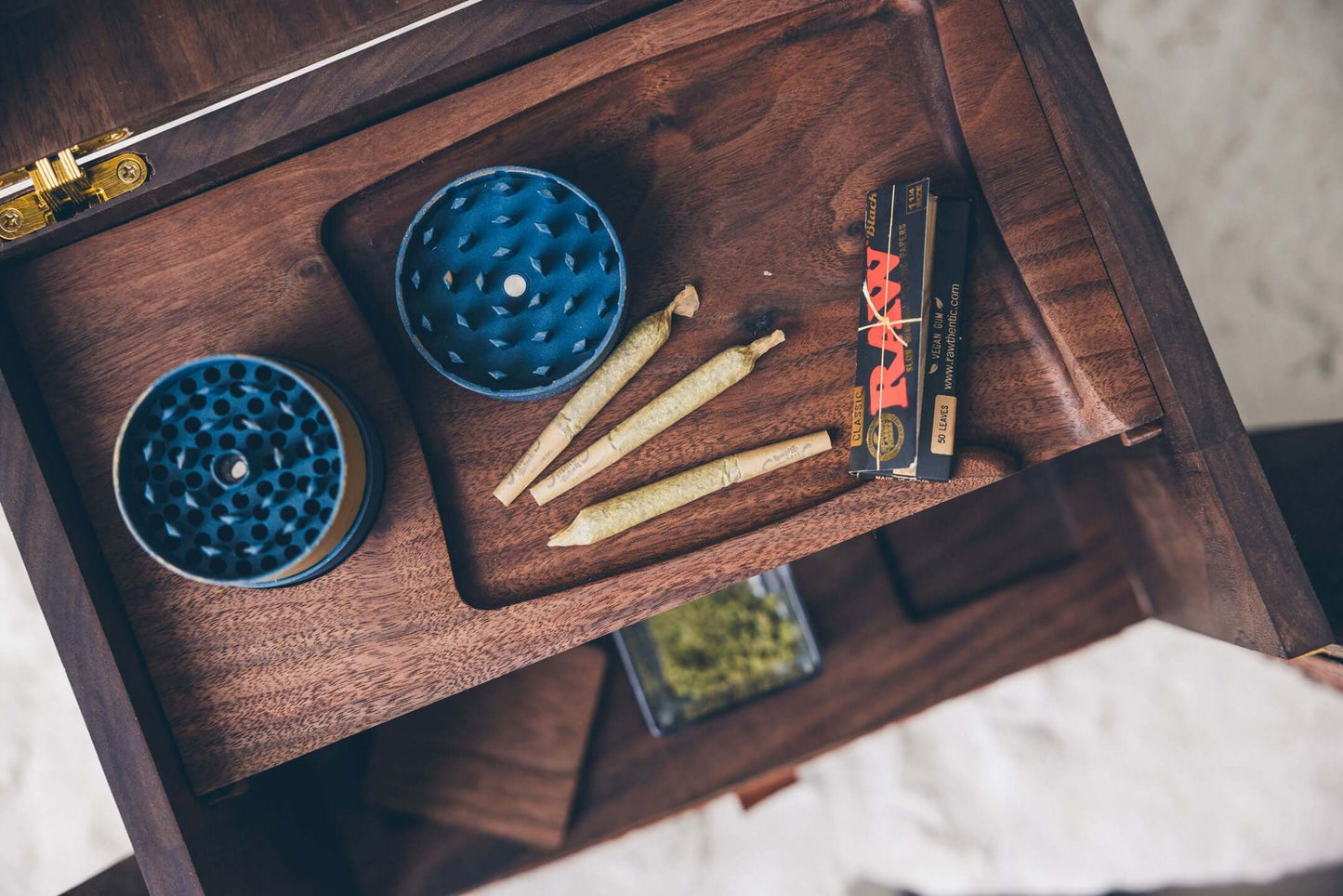 Wooden drawer with marijuana accessories: blue grinders, rolled joints, and RAW papers.