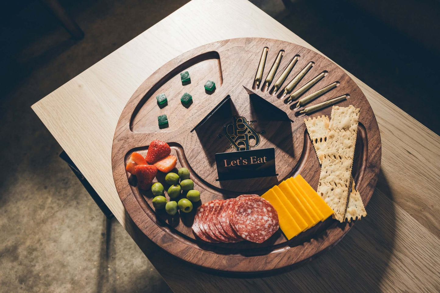 Wooden platter with cheese, salami, crackers, fruits, and a decorative 'Let's Eat' box.