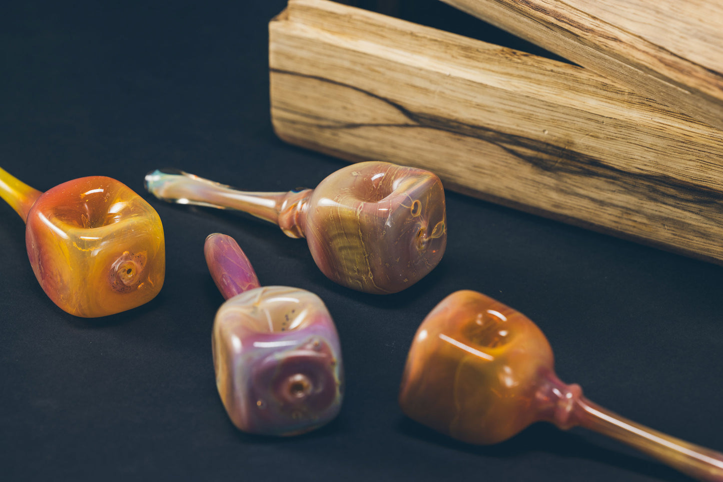 Colorful handmade glass pipes displayed on a dark surface with wooden background.